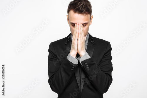 Focused businessman, in black suit, holding hands together, praying, on white background