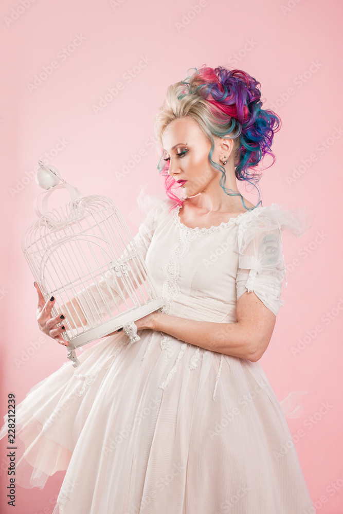 Stylish girl in white dress. Creative hair coloring. Multi-colored hairstyle. Concept with an empty bird cage.