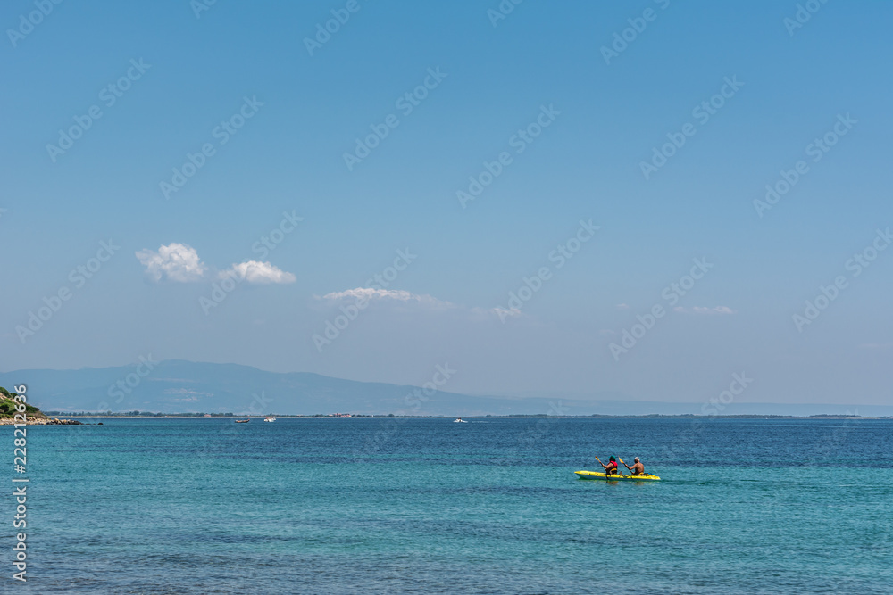 One yellow kayak with unrecognizable people at an open turquoise sea on a sunny summer day in Sardinia, Italy. 