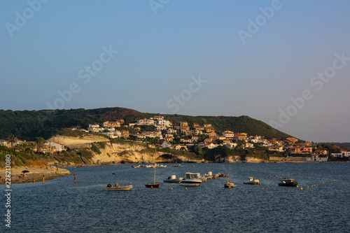 Beach of S`Archittu di Santa Caterina, Oristano Province, Sardinia, Italy with boats and lot of unrecognizable people on the beach.