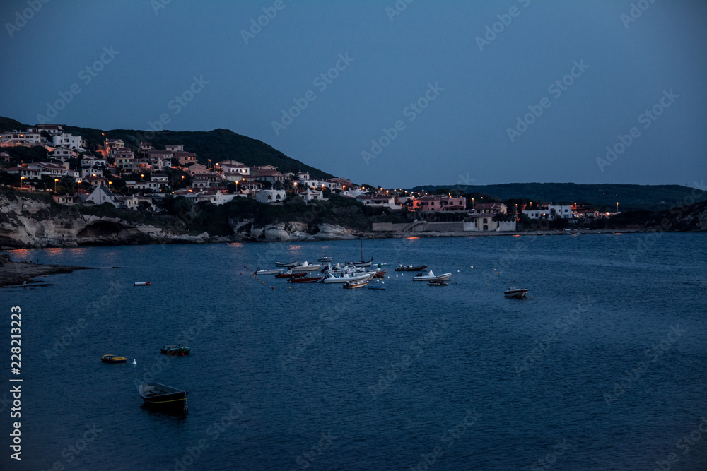 Beach of limestone rock S`Archittu di Santa Caterina, Oristano Province, Sardinia, Italy captured at blue hour with boats in the water.