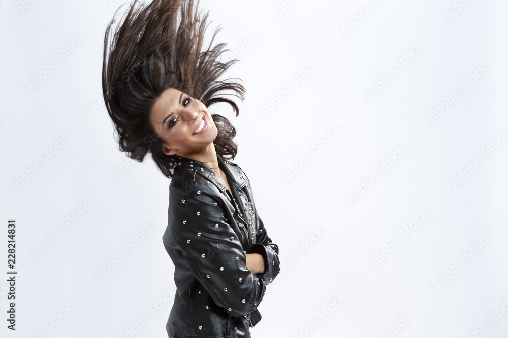 Fashion and Lifestyle Ideas and Concepts. Portrait of Smiling Caucasian Brunette Girl in Rough Leather Jacket Making Waving Hair Against White. Fashion and Lifestyle Ideas and Concepts. Portrait of Smiling Caucasian Brunette Girl in Rough Leather Jacket Making Waving Hair Against White.