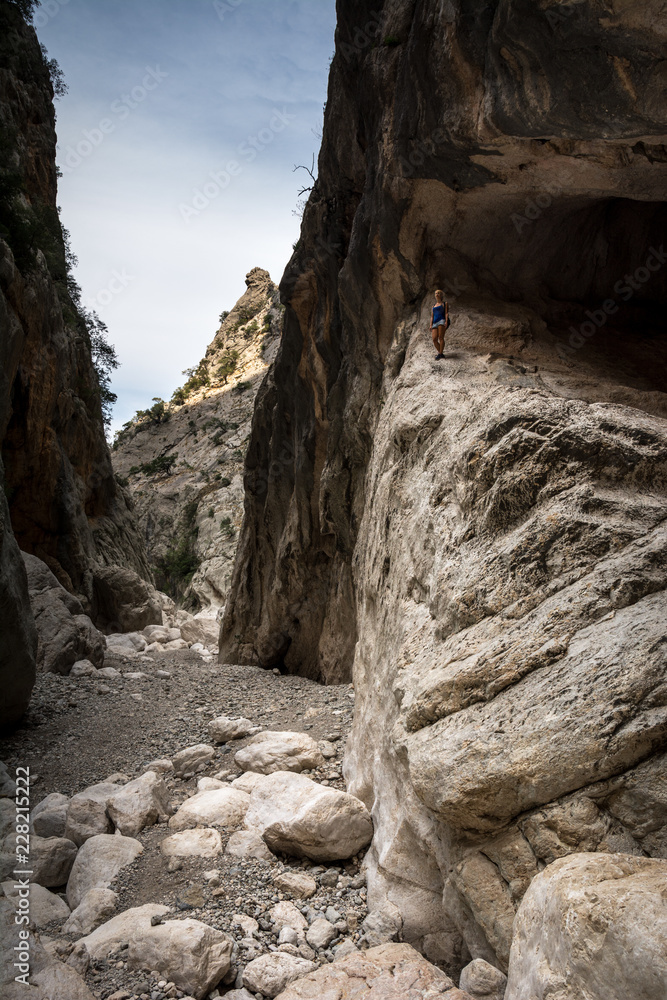 Young woman standing in the background of canyon and looking far away. Shot in Gola Su Gorropu canyon, Sardinia, Italy - important natural site in Sardinia.