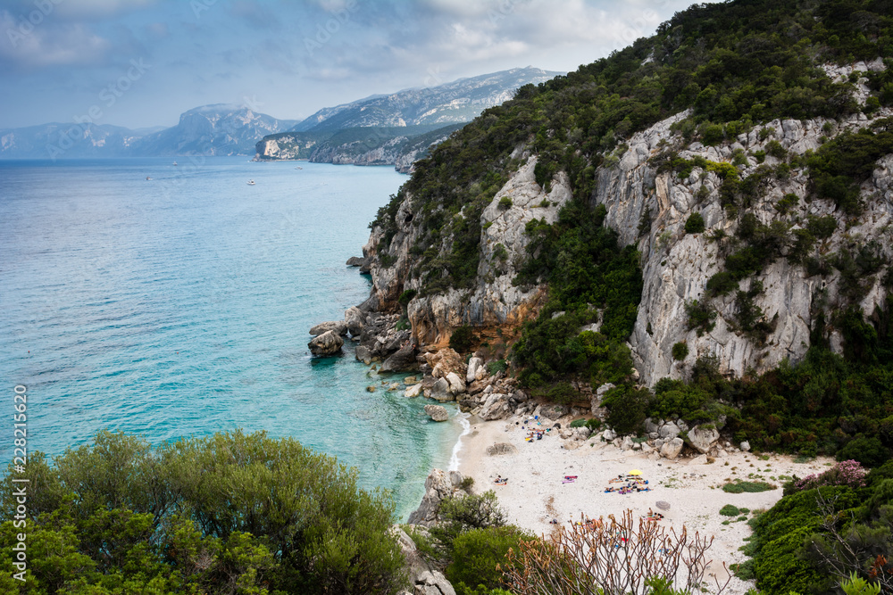Cala Gonone beach in Sardinia with unrecognizable people on an overcast summer day, perfect vacation place. Seascape view. Cala Gonone beach in Sardinia with unrecognizable people on an overcast summer day, perfect vacation place. Seascape view.