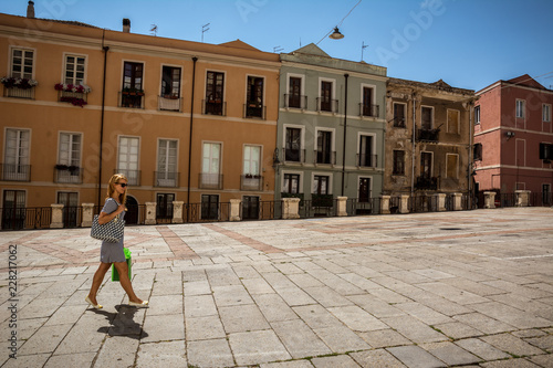 Beautiful young woman with blond hair and shopping bags in her hands is walking through Cagliari downtown  streets in Sardinia, Italy. 