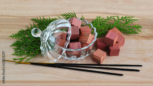 Fragrant wardrobe freshener cubes made of natural pencil cedar wood in a crystal bowl with a lid, few green cypress sprigs and few incense sticks on a wooden background, view from above photo