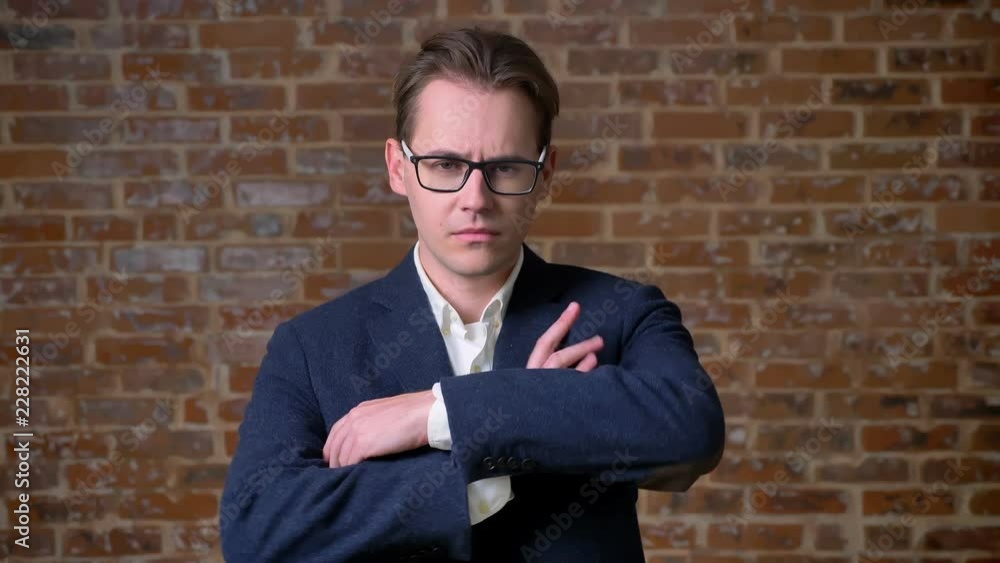 Serious caucasian man in business suit and glasses standing and looking at camera focused in red brick studio isolated Serious caucasian man in business suit and glasses standing and looking at camera focused in red brick studio isolated