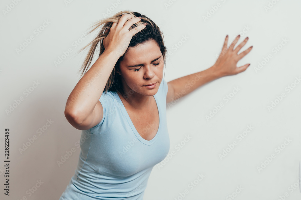 Woman suffering from dizziness with difficulty standing up while leaning on wall Woman suffering from dizziness with difficulty standing up while leaning on wall