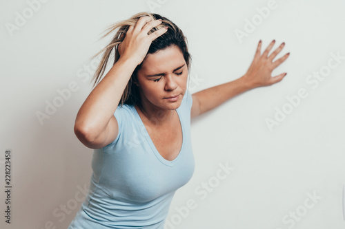 Woman suffering from dizziness with difficulty standing up while leaning on wall