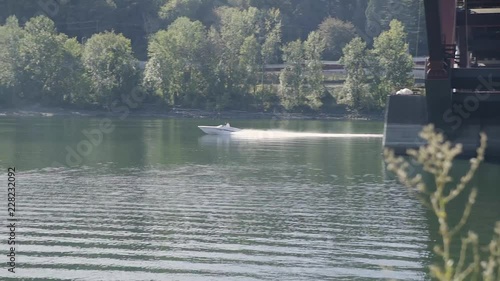 small speed boat appears from behind bridge and continues up river creating a wake. photo