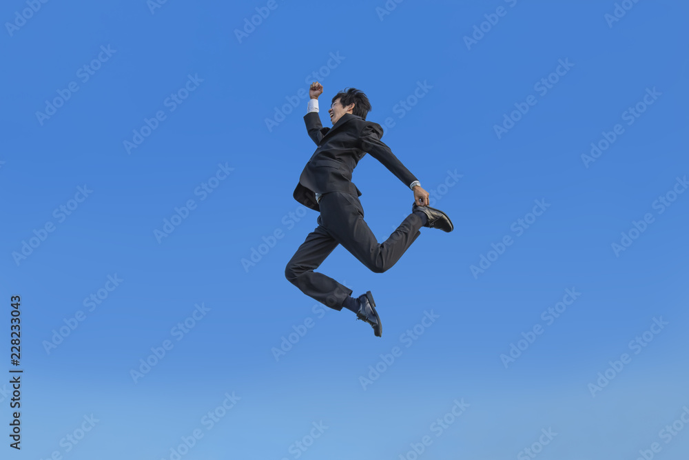 青空をバックに空中を走るスーツ姿の若いビジネスマン1人。元気・健康・発展・挑戦イメージ