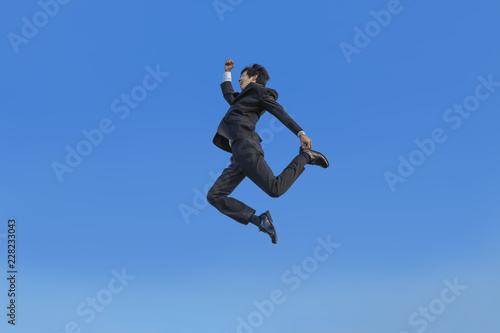 青空をバックに空中を走るスーツ姿の若いビジネスマン1人。元気・健康・発展・挑戦イメージ