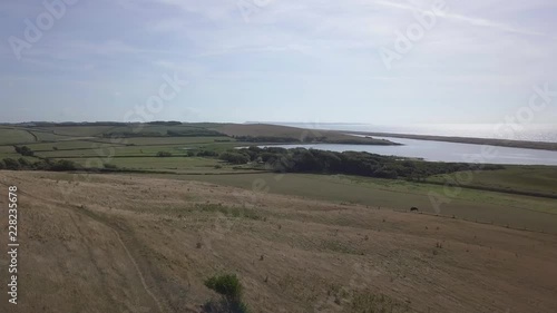 Low forward tracking aerial down a hill towards the fleet lagoon at the west end of Chesil Beach. Abbotsbury, Dorset. photo