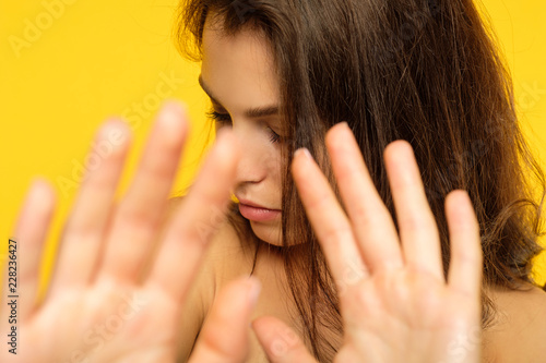 blocking the world and shutting out something. denial refusal and rejection concept. girl putting hands forward covering from view. portrait of young woman on yellow background.