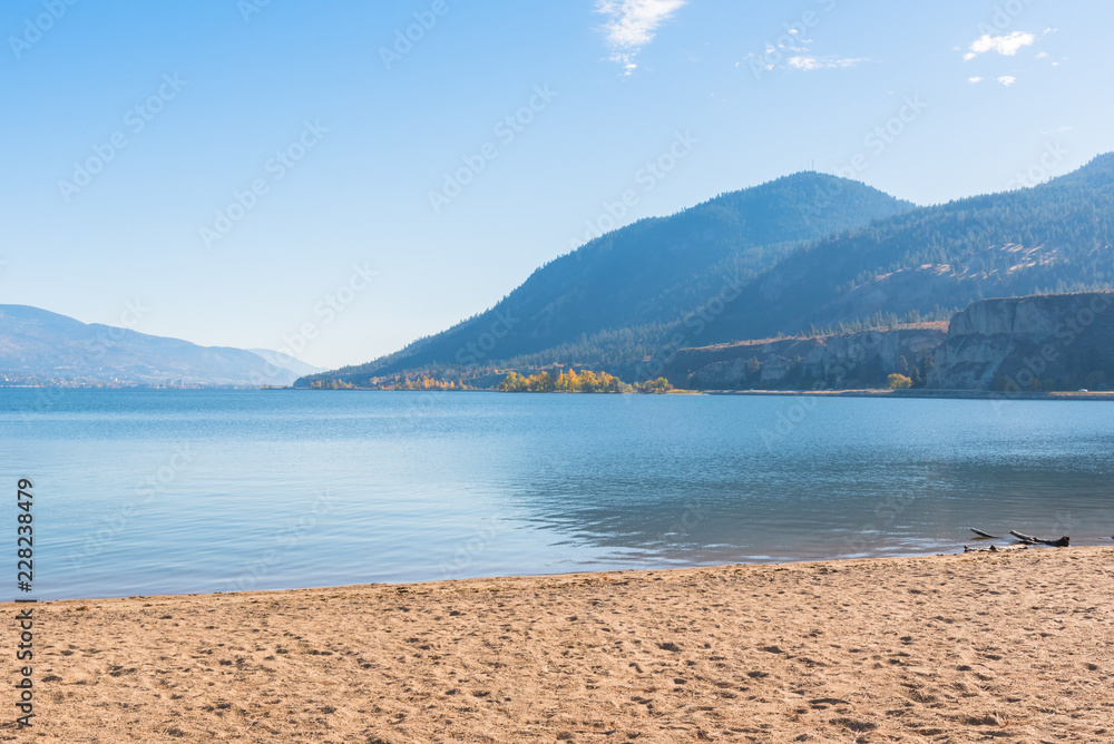 Lake with sandy beach, mountains, and blue sky