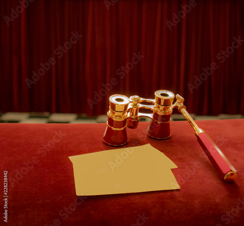 Vintage opera glasses and blank tickets at background of drop-curtain in theatre photo
