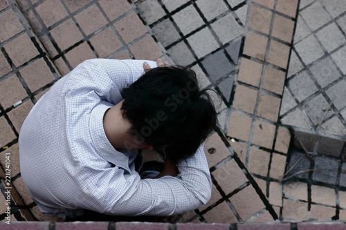 Aerial view of sad stressed young Asian business man suffering from severe depression. Thoughtful concept