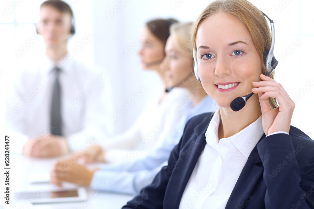 Group of call center operators at work. Focus at blonde beautiful business woman in headset Group of call center operators at work. Focus at blonde beautiful business woman in headset