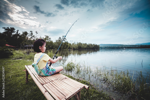Happy girl pulling rod while fishing against landscape of lake.