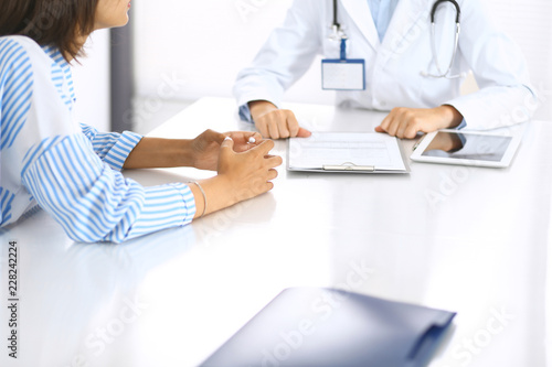 Doctor and patient talking and discussing health treatment while sitting at the desk, close-up. Medicine and health care concept