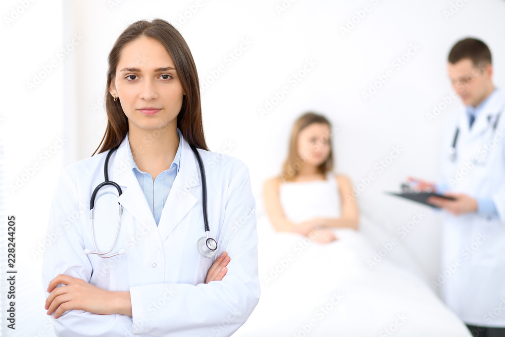 Medicine doctor standing and smiling on the background with patient in the bed Medicine doctor standing and smiling on the background with patient in the bed