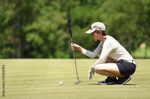 Woman golfer check line for putting golf ball on green grass