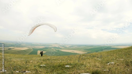 medium shot professional paraglider pilot prepares for takeoff raises the wing and walks with the wing raised along the paradrome photo