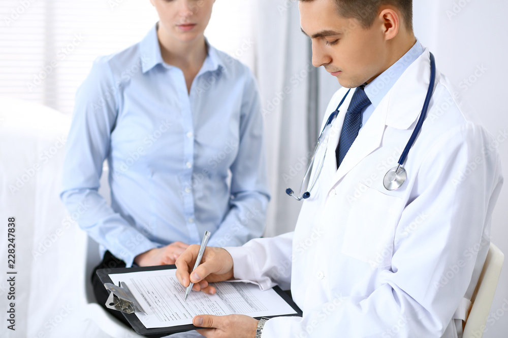 Male doctor holding application form while consulting female patient in hospital. Perfect service in medicine and healthcare concept Male doctor holding application form while consulting female patient in hospital. Perfect service in medicine and healthcare concept