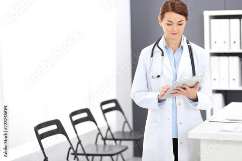 Happy doctor woman at work. Portrait of female physician using tablet computer while standing near reception desk at clinic or emergency hospital. Medicine concept