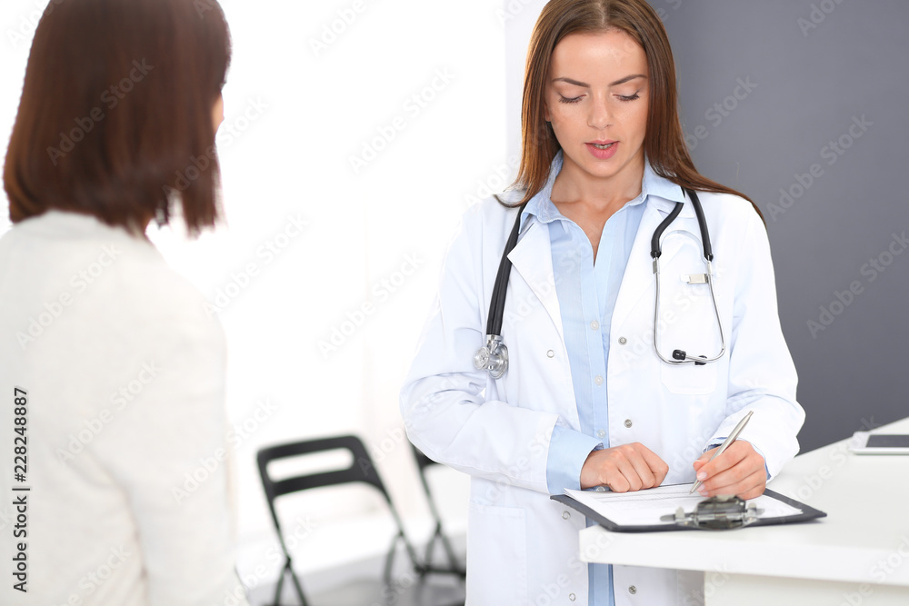 Doctor and patient discussing something while standing near reception desk in emergency hospital. Physician at work in clinic. Medicine and health care concept Doctor and patient discussing something while standing near reception desk in emergency hospital. Physician at work in clinic. Medicine and health care concept