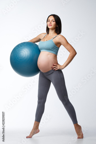 Slim pregnant woman is engaged in fitness with a ball isolated on a white background.