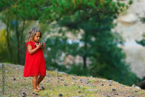 Little girl in a red dress collects cones in the forest