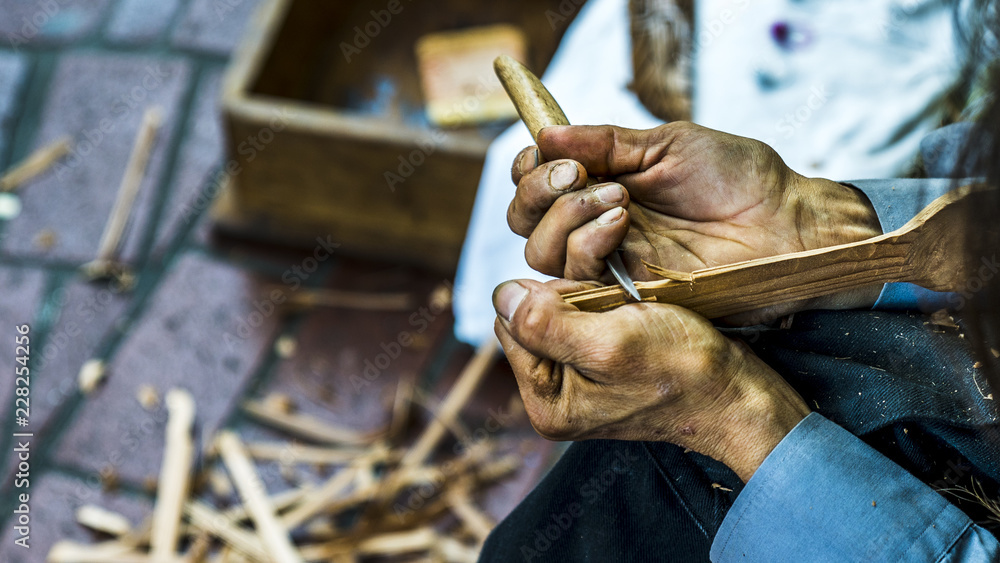 Obraz premium Native woman carving wood on the streets of Vancouver British Columbia, Canada. Shaping a piece of wood into a spoon with Native elements engraved.