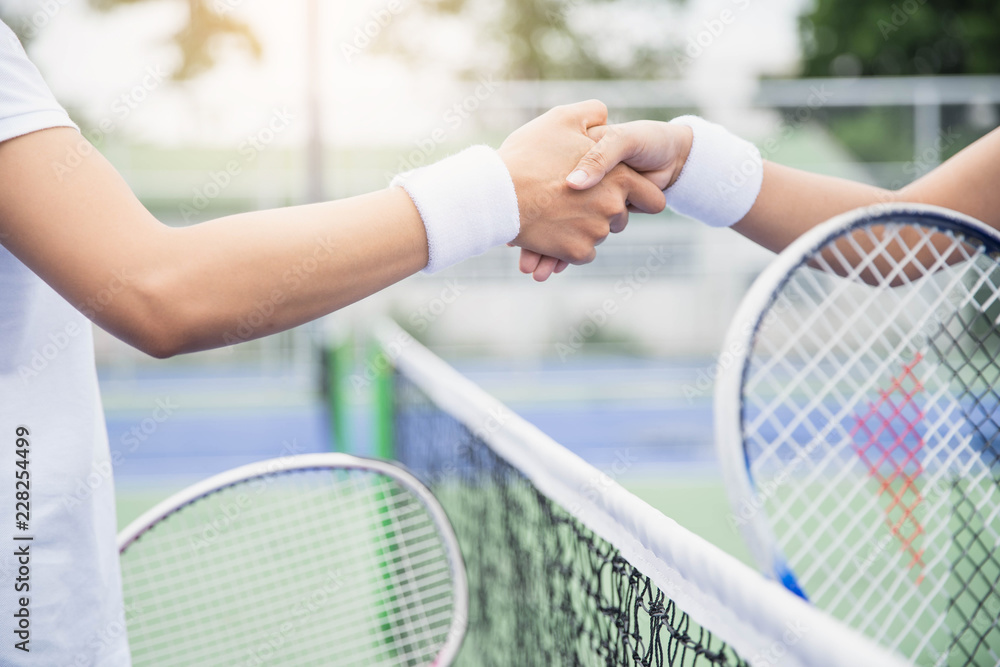 Women tennis player handshaking after playing a tennis match. Handshake at tennis court - agonism,respect,fair play,sport concept.
