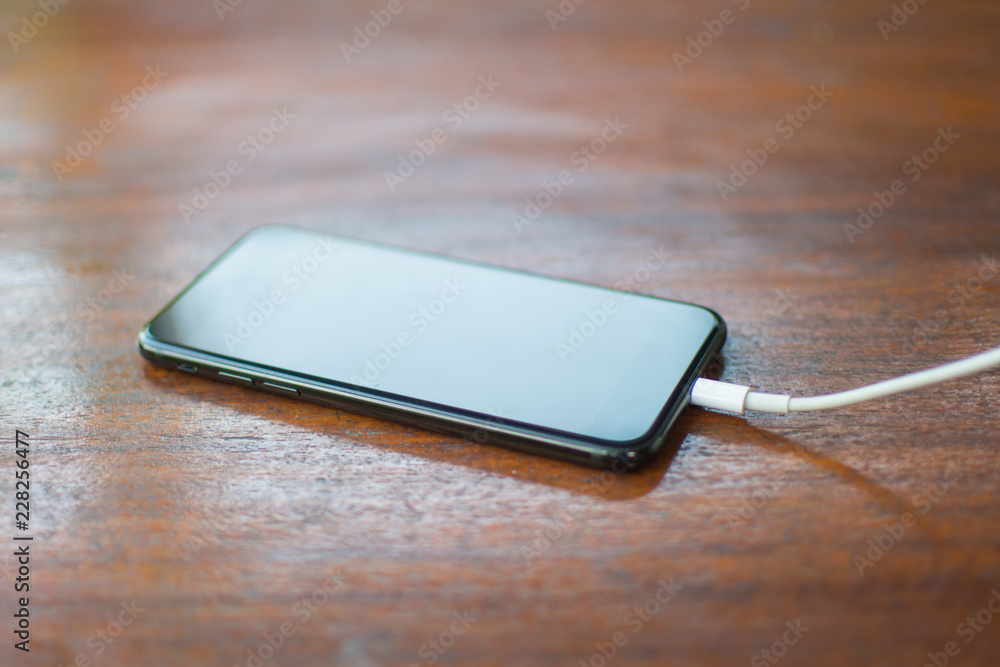 Black smartphone with cable charge on wooden table. subject is blurred. Black smartphone with cable charge on wooden table. subject is blurred.