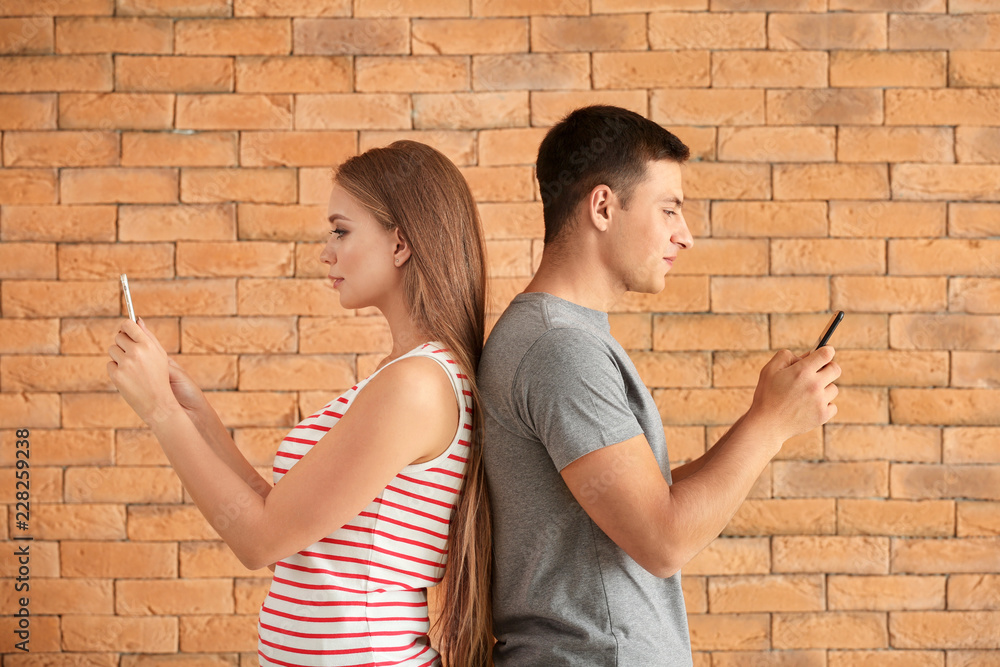 Young couple with mobile phones against brick wall Young couple with mobile phones against brick wall
