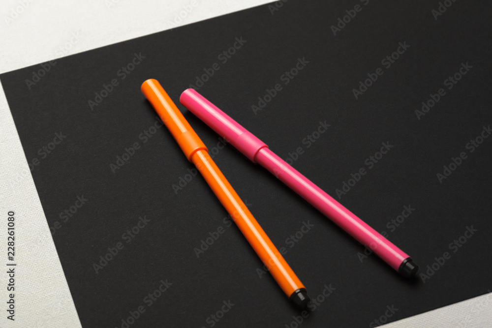 Two felt-tip pens of pink and orange colors on black paper background Two felt-tip pens of pink and orange colors on black paper background