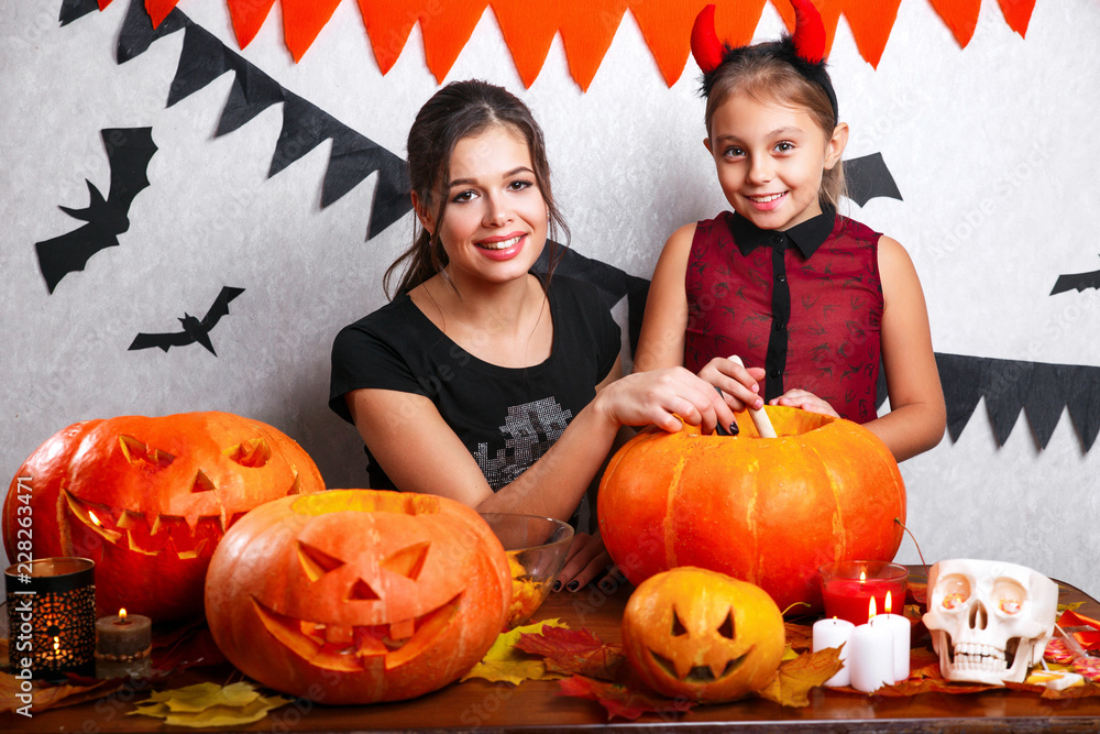 Fototapeta premium Happy Halloween! Mother and daughter carving pumpkin. Family preparing for holiday.