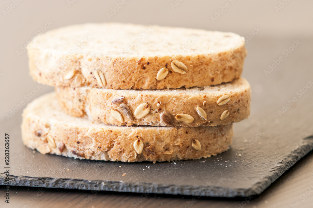 Slices of homemade multigrain bread on black slate board Slices of homemade multigrain bread on black slate board