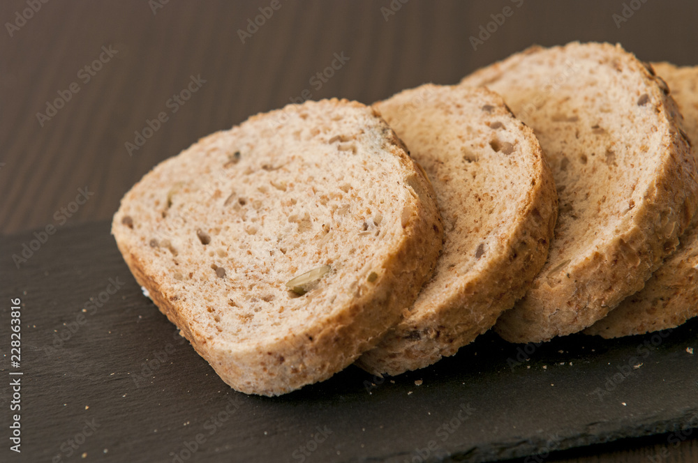 Slices of homemade multigrain bread on black slate board Slices of homemade multigrain bread on black slate board