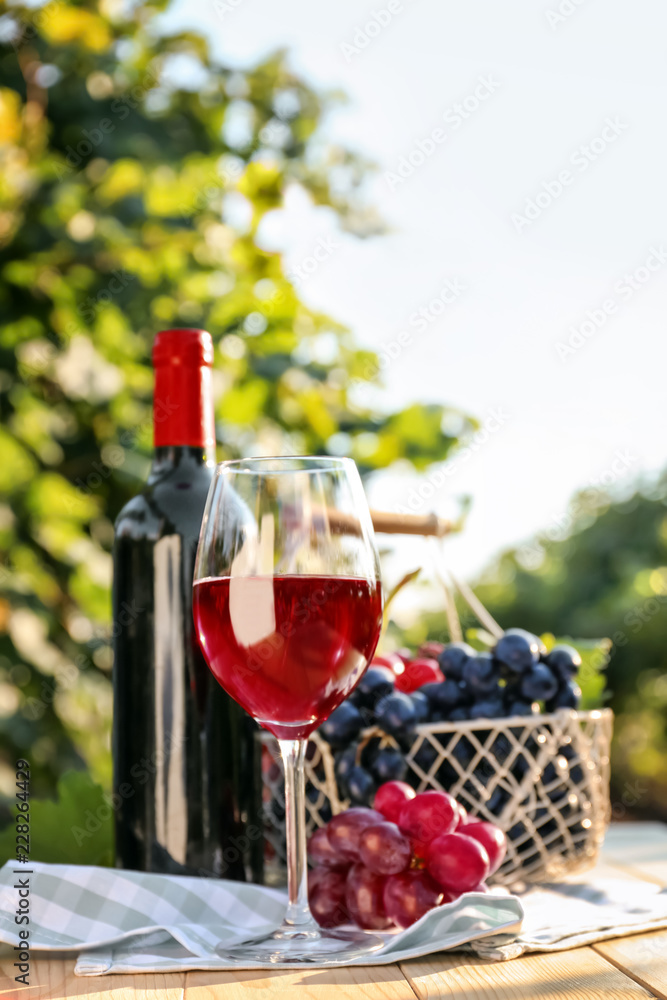 Glass and bottle of red wine with fresh grapes on wooden table in vineyard