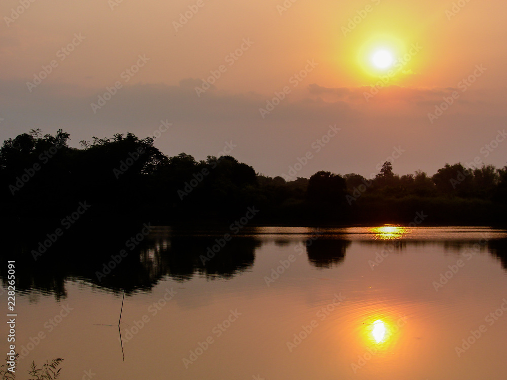Beautiful yellow sunset over the river and pond with trees and forest in silhouette background.