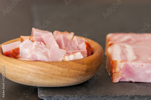 Pieces of baked ham in bowl on black slate board, close-up