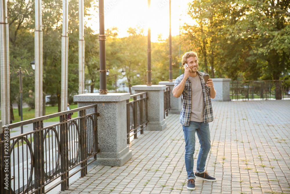 Handsome young man with coffee talking on mobile phone in park Handsome young man with coffee talking on mobile phone in park