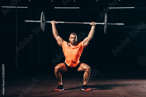 handsome fit man working out with barbell in dark gym