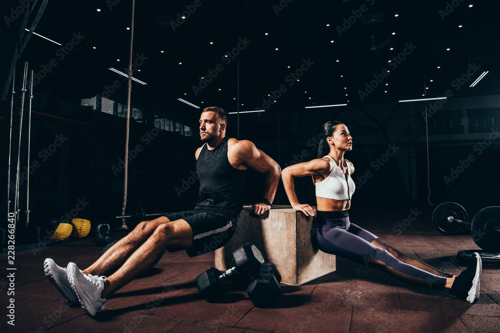 Fototapeta premium Athletic sportsman and sportswoman exercising on cube together in dark gym
