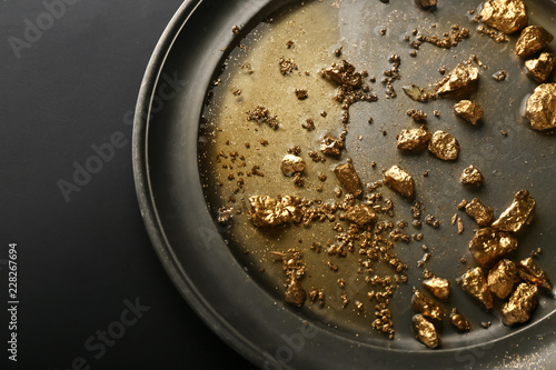 Plate with gold nuggets on black background
