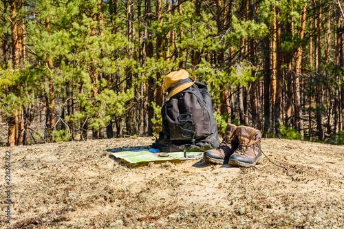 Backpack, touristic boots, map, compass and hat on a ground in a coniferous forest