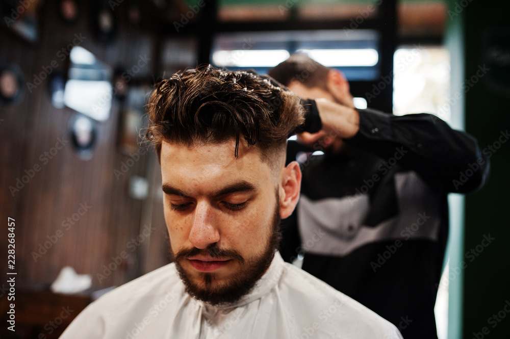 Obraz premium Handsome bearded man at the barbershop, barber at work.