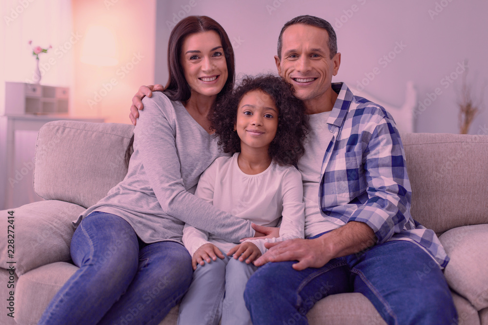 Family happiness. Nice happy family sitting together on the sofa while smiling to you Family happiness. Nice happy family sitting together on the sofa while smiling to you